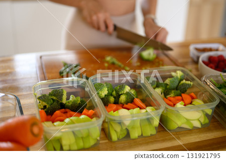 Woman preparing fresh vegetables for healthy meal prep, organizing colorful ingredients in containers Woman preparing fresh vegetables for healthy meal prep, organizing colorful ingredients in containers 131921795
