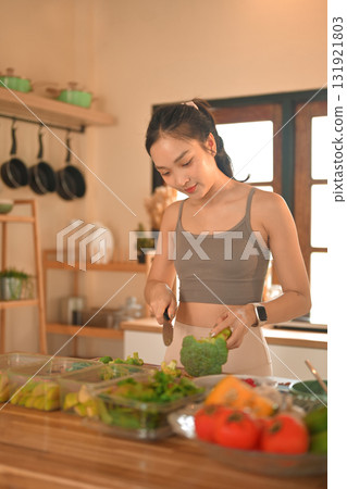 Asian woman in sportswear cutting vegetables for nutritious meal in a kitchen Asian woman in sportswear cutting vegetables for nutritious meal in a kitchen 131921803