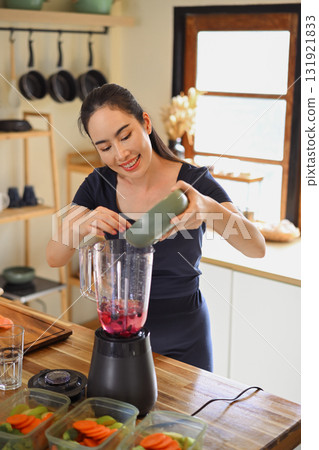 Smiling woman preparing fresh smoothie with berries in blender, enjoying healthy lifestyle in modern kitchen 131921833