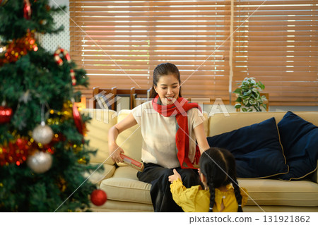 Happy mother giving a Christmas present to her daughter while sitting on the sofa near a decorated tree 131921862