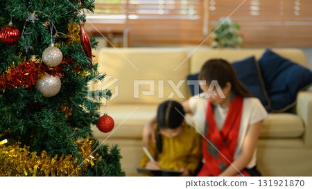 Close up of decorated Christmas tree with blurred background of mother and daughter using tablet together 131921870