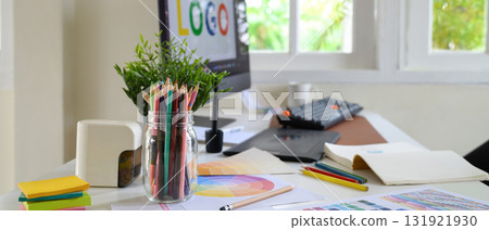 creative designer workspace with colored pencils in a jar, color palettes, and computer screen displaying a logo design creative designer workspace with colored pencils in a jar, color palettes, and computer screen displaying a logo design 131921930