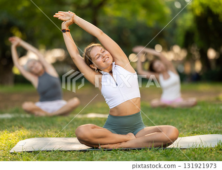 Girl stretching in lotus position at group yoga class outdoors 131921973