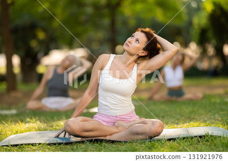 Woman doing neck stretching exercises in lotus pose in summer park Woman doing neck stretching exercises in lotus pose in summer park 131921976
