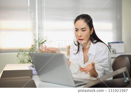 Frustrated woman looking at laptop screen, expressing confusion and stress while working in the office. 131921987