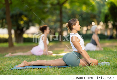 Active happy woman in sportswear sitting on yoga mat and doing stretching legs during yoga class in green park at daytime Active happy woman in sportswear sitting on yoga mat and doing stretching legs during yoga class in green park at daytime 131922002