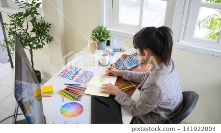 Female graphic designer sketching a colorful logo design in a notebook 131922003