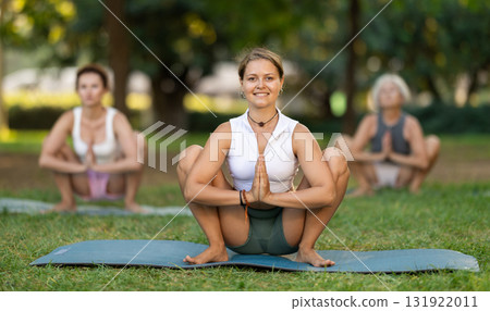 Girl performing Garland Pose during group yoga in park 131922011