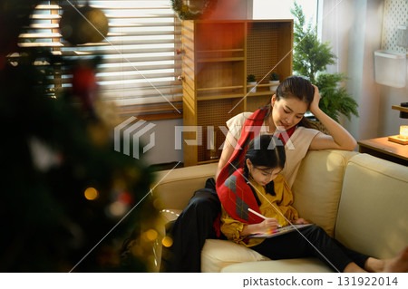 Mother and daughter sitting on sofa using tablet together in cozy living room decorated for Christmas Mother and daughter sitting on sofa using tablet together in cozy living room decorated for Christmas 131922014