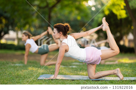 Woman performing stretching Vyaghrasana asana in outdoor group yoga session Woman performing stretching Vyaghrasana asana in outdoor group yoga session 131922016