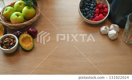 Flat lay of healthy fresh fruits, avocado, nuts, and berries arranged around wooden table with copy space Flat lay of healthy fresh fruits, avocado, nuts, and berries arranged around wooden table with copy space 131922024