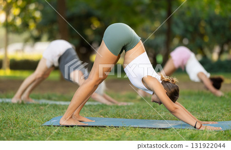 Diligent women practicing feet apart forward bend pose of yoga on mat at city park together Diligent women practicing feet apart forward bend pose of yoga on mat at city park together 131922044