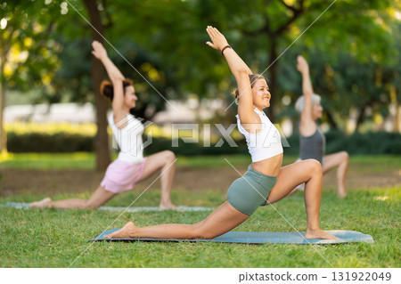 Girl doing Crescent Low Lunge Pose during group outdoor yoga class 131922049