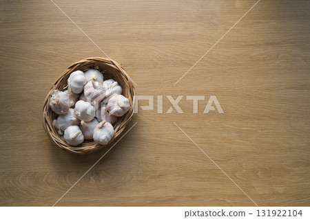 Top view of a wicker basket filled with fresh garlic bulbs placed on a wooden table Top view of a wicker basket filled with fresh garlic bulbs placed on a wooden table 131922104