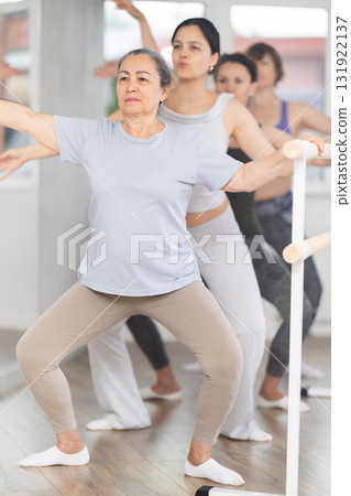 Women doing ballet at group amateurs training session in the studio performs demi plie near the ballet barre, standing in ballet stance 131922137