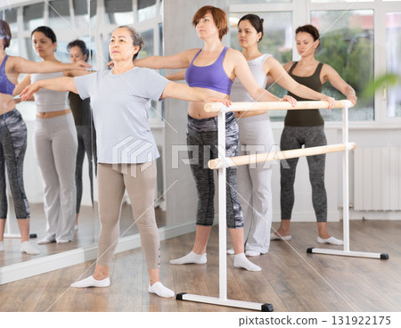 Women of different ages exercise near the ballet barre at group training session in batman batyu position Women of different ages exercise near the ballet barre at group training session in batman batyu position 131922175