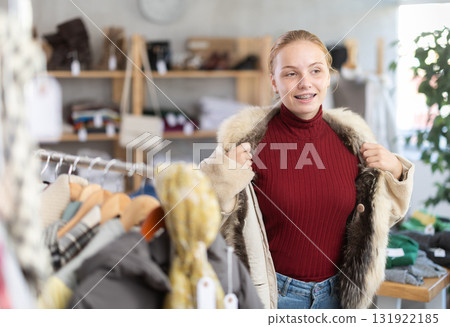 Positive teen girl trying on fur coat in clothing store 131922185