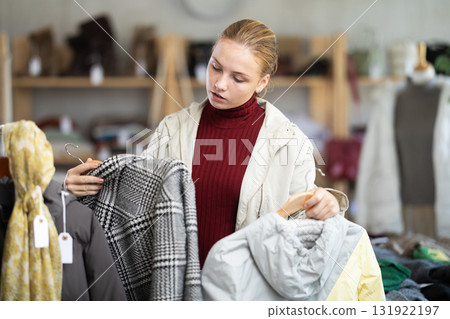 While shopping, teen girl browsing goods items and choose elect down jacket in store 131922197
