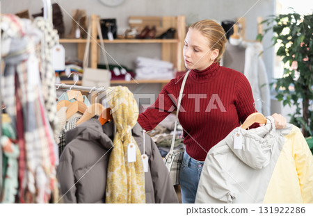 Attentive teenage girl choosing lightweight jacket in clothing store 131922286