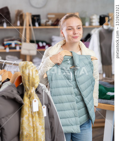 Positive teen girl choosing light green vest in clothing store 131922321