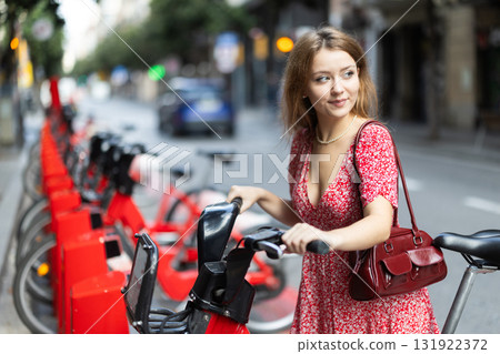 young woman stands near a bicycle rental point young woman stands near a bicycle rental point 131922372