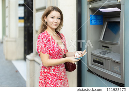Woman uses ATM, withdraws cash from card. Girl buys travel ticket from machine 131922375