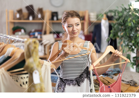 Young woman chooses a set of clothes for the summer. Visitor to the boutique examines new summer collection of clothes 131922379