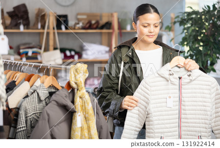 Asian woman standing in clothing shop and looking new down jacket made of high-quality material. Shopping and seasonal sales concept, autumn-winter season 131922414