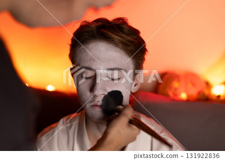 A person is applying white makeup preparing for a Halloween-themed look. 131922836