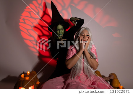 Woman in pink dress with witch costume laughing in front of Halloween decoration Woman in pink dress with witch costume laughing in front of Halloween decoration 131922971