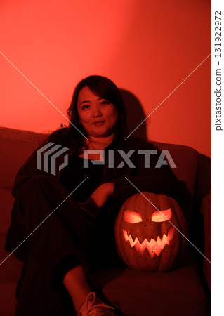 Woman sitting on couch, holding pumpkin, smiles warmly, autumn vibes 131922972