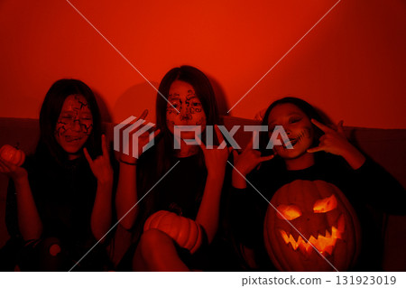 friends are celebrating Halloween,posing with a pumpkin and making devil horns friends are celebrating Halloween,posing with a pumpkin and making devil horns 131923019
