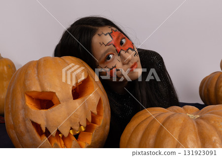 Girl with face painted like a pumpkin,smiling brightly in costume for Halloween 131923091