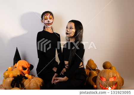 women in Halloween costumes sitting on pumpkins,surrounded by festive decoration women in Halloween costumes sitting on pumpkins,surrounded by festive decoration 131923095