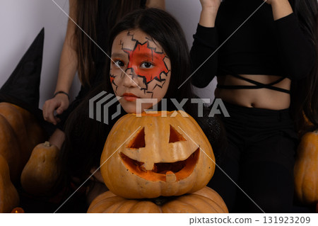 A person with a painted face is posing with a carved pumpkin for Halloween A person with a painted face is posing with a carved pumpkin for Halloween 131923209