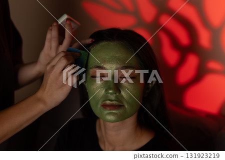 The model is getting her face painted green for a Halloween costume 131923219