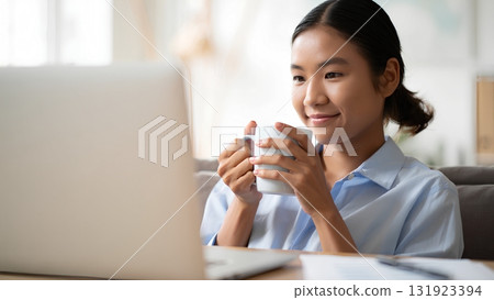 Side view of woman drinking coffee while working on her laptop, remote work and digital nomad lifestyle concept 131923394