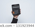 Man hand in black shirt holding modern black digital calculator with LCD display against loght background. Business and finance tool for commercial and educational use. 131923944
