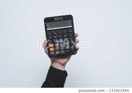 Man hand in black shirt holding modern black digital calculator with LCD display against loght background. Business and finance tool for commercial and educational use. 131923944
