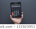 Man hand holding black digital calculator displaying 2025 on LCD screen against gray background. Business finance and annual planning concept for new year calculations and budgeting. 131923951