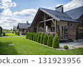Blurred modern wooden house exterior, nestled amidst lush green grass and manicured bushes under a bright sky. 131923956