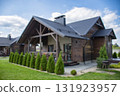 Blurred modern wooden house exterior, nestled amidst lush green grass and manicured bushes under a bright sky. 131923957