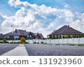 Blurred view of a quiet suburban neighborhood with private houses, white fences, and a curved street under a cloudy sky. Background for real estate, property, and urban development themes. 131923960
