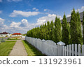 Blurred view of a quiet suburban neighborhood with private houses, white fences, and a curved street under a cloudy sky. Background for real estate, property, and urban development themes. 131923961