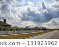 Blurred view of a quiet suburban neighborhood with private houses, white fences, and a curved street under a cloudy sky. Background for real estate, property, and urban development themes. 131923962
