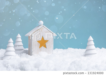 A white wooden toy house with wooden Christmas trees in the snow. 131924000