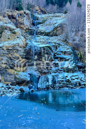 Majestic frozen waterfall cascading over rocky cliffs under a clear sky in winter Majestic frozen waterfall cascading over rocky cliffs under a clear sky in winter 131924078