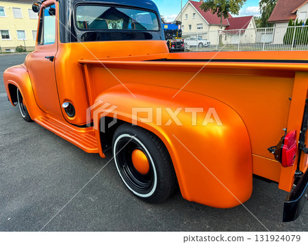 Classic vintage truck shines bright in vibrant orange under the sun in a bustling urban setting 131924079