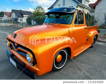 Vintage orange pickup truck parked on a sunny day in a suburban neighborhood with modern homes in the background 131924080