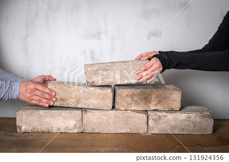 Two people placing bricks together to build a wall. Symbol of teamwork, progress and stability in 131924356